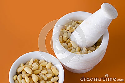 Shelled pine nuts in bowl and mortar over orange Stock Photo