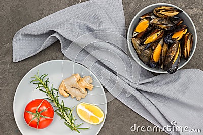 Shellfish mussels in shells in gray bowl. Rosemary, lemon and ginger in gray plate. Gray napkin Stock Photo