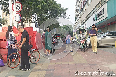 Shenzhen, China: a street view of elderly people waiting for tour buses and women on bicycles Editorial Stock Photo