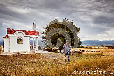 A shepherd in front of a little chapel and a herd of sheep Editorial Stock Photo