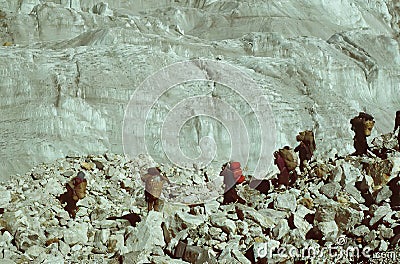 Sherpa porters carry loads beneath huge glacier Editorial Stock Photo