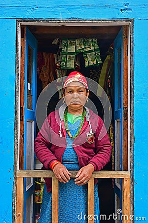 Nepalese Sherpa woman in traditional attire standing at front blue door along Everest Base Camp village, Nepal Editorial Stock Photo