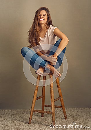 Shes just what you need on a cloudy day. Studio shot of a beautiful young woman sitting on a stool against a plain Stock Photo