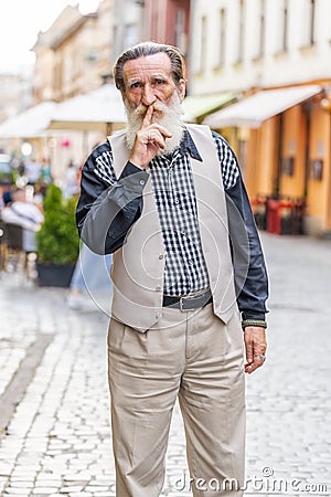 Senior man presses finger to lips makes silence hush sign do not tells gossip secret quiet in city Stock Photo