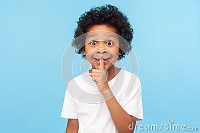 Shh, be quiet! Portrait of funny cute little boy with curly hair in T-shirt making silence gesture with finger on his lips Stock Photo