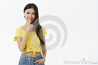 Shh keep it between us. Charming mysterious and flirty young woman in trendy yellow t-shirt making shush gesture with Stock Photo