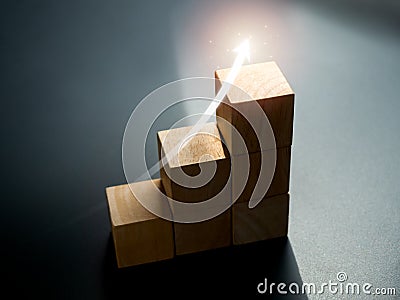 Shining rise up arrow on wooden cube blocks, bar graph chart steps on dark background. Stock Photo