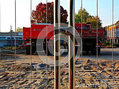 Shiny galvanized steel mesh construction hoarding and trucks beyond Stock Photo