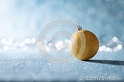 Shiny Gold Christmas Bauble in Winter Wonderland. Blue Christmas background with defocused christmas lights. Stock Photo