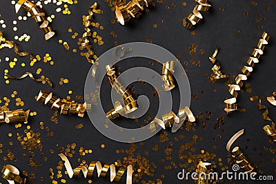 Shiny golden serpentine streamers and confetti on black background, flat lay Stock Photo