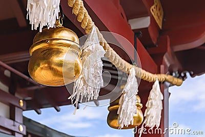 Shiny golden suzu bells hung on a shimenawa straw rope adorned with shide paper in a Shinto shrine. Editorial Stock Photo