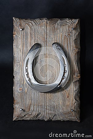 A shiny metal horseshoe, nailed to an old board with forged key holder nails Stock Photo