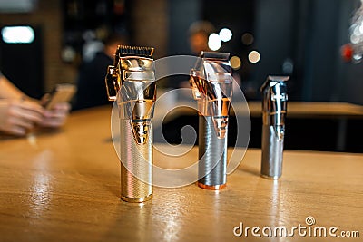 Shiny metallic vintage hair trimmers stand on a wooden table in a men`s hair salon. Male barbershop. Stock Photo