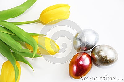 Shiny multicolored easter eggs and yellow tulips with green leaves Stock Photo