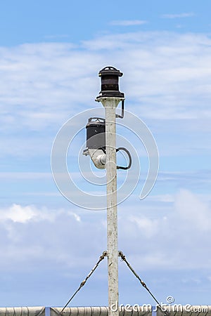 Ship`s stern light post with two lights against cloudy blue sky. Turnbuckles and steel wires are holding the pole upright Stock Photo