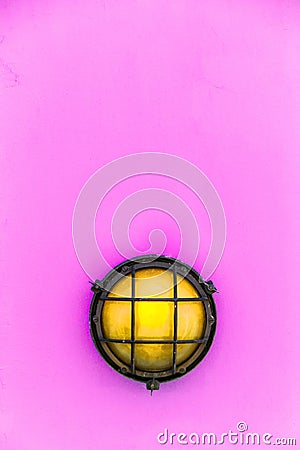 Ship yellow deck lamp bulkhead light surrounded by a metal rusted frame fixed to a painted light pink wall Stock Photo