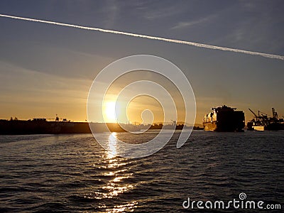 Shipping boat pulled by tugboats out of harbor as Shipping boat is unloaded by cranes in Oakland Harbor at sunset Editorial Stock Photo