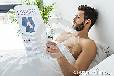 shirtless bearded man reading business newspaper in bed Stock Photo