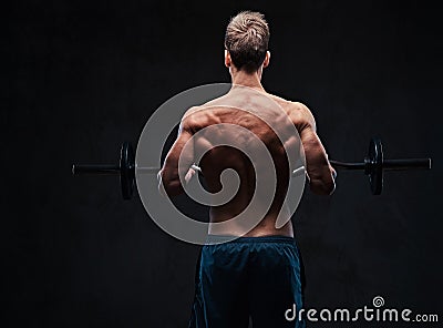 Shirtless male holds barbell over dark grey background. Stock Photo