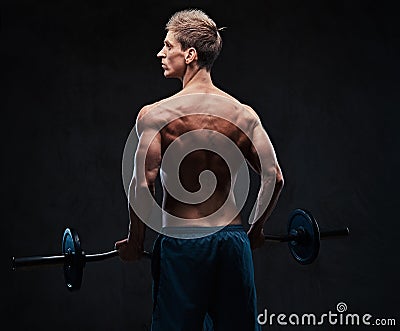 Shirtless male holds barbell over dark grey background. Stock Photo