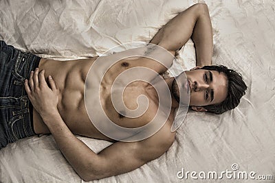 Shirtless male model lying alone on his bed Stock Photo