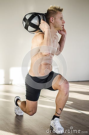 Shirtless young man in gym holding water-filled weight in his hands Stock Photo