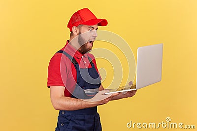 Shocked astonished handyman standing laptop in hands and working online, getting huge order. Stock Photo