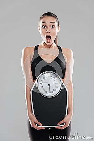 Shocked astonished young woman athlete holding weighing scale Stock Photo