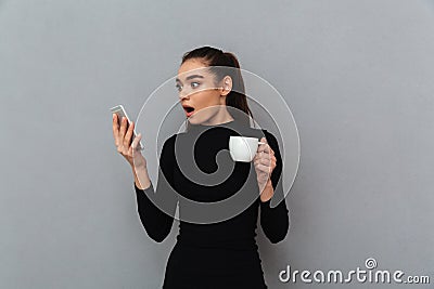 Shocked brunette woman in black clothes looking at smartphone Stock Photo