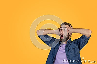 Shocked Caucasian man screaming and grabbing his head in disbelief, looking at blank space on orange studio background Stock Photo