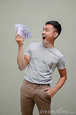 Shocked and excited Asian man holding USD dollar bills, standing against a green studio background Stock Photo