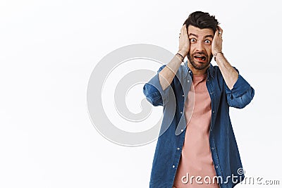 Shocked freak-out, alarmed young bearded guy, scream in panic grab head in hands and stare camera scared, anxious about Stock Photo