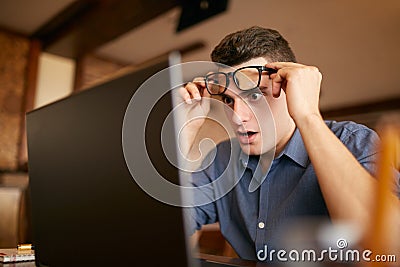 Shocked freelancer hipster man looks to laptop screen and can not believe unpleasant news. Pop-eyed frightened Stock Photo