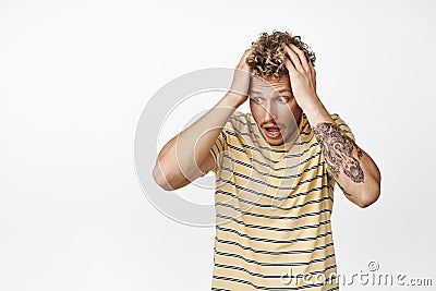 Shocked and frustrated blond young man ripping his hair on head and staring aside, reaction to disaster, panic during Stock Photo
