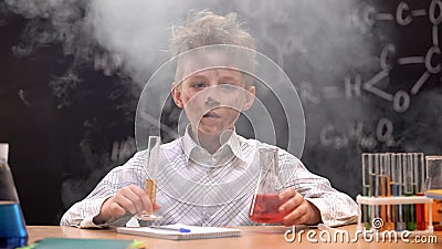 Shocked funny dirty schoolboy holding chemical tube and flask, smoke around him Stock Photo