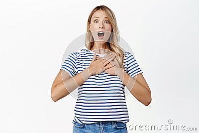 Shocked girl screams and looks startled, holds hands on heart, jumping frighetened, being scared, standing over white Stock Photo