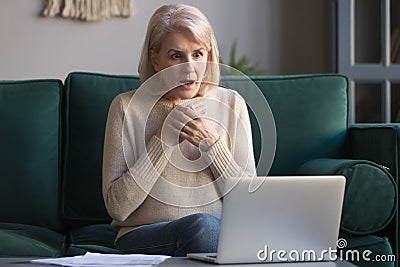 Shocked grey haired mature woman reading unexpected news on laptop Stock Photo