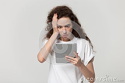 Shocked millennial woman touching head, holding digital tablet. Stock Photo