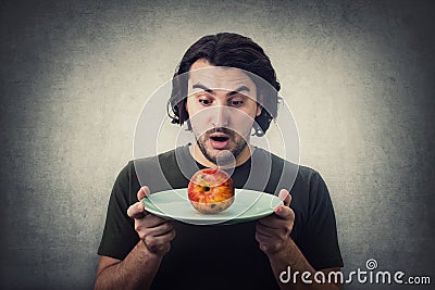 Shocked person holding dish plate a slightly degraded apple, rotten fruit. People has no food to eat after drought. Global crisis Stock Photo