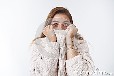 Shocked scared stunned cute caucasian woman hiding face collar sweater pulling cloth nose widen eyes amazed speechless Stock Photo