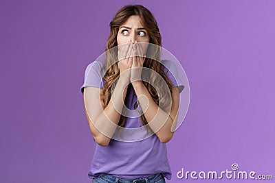 Shocked timid insecure concerned curly-haired woman look sideways stunned scared gasping cover mouth hold palms pressed Stock Photo