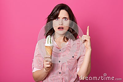 Shocked unsatisfied model opening her mouth and eyes widely with surprise, raising forefinger, having indignation, looking Stock Photo