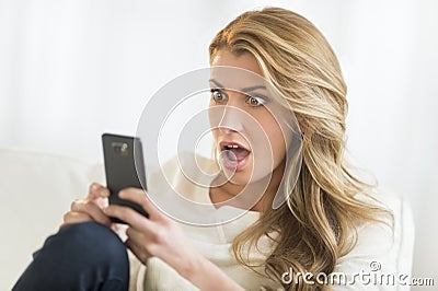 Shocked Woman Looking At Mobile Phone At Home Stock Photo