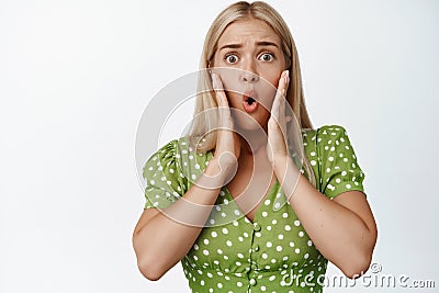 Shocked and worried blond woman looking concerned, reacting to bad terrible news, staring troubled against white Stock Photo
