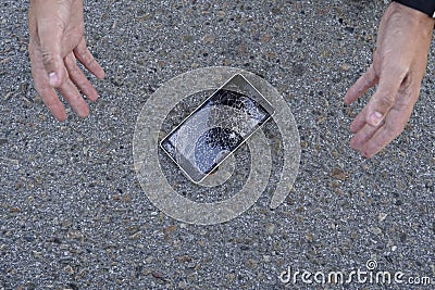 Shocked young man throws up her hands, her phone fell and crashed. Broken smartphone with cracked screen glass lays on Stock Photo