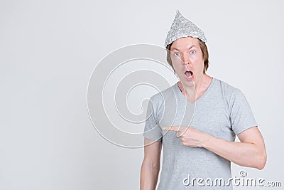 Shocked young man with tinfoil hat as conspiracy theory concept pointing to side Stock Photo