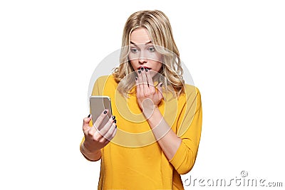 Shocked young woman holding up her mobile phone, reading shocking news. Woman in disbelief, isolated over white background. Stock Photo