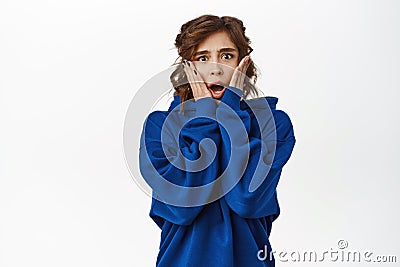 Shocked young woman, horrified, looking scared or worried, standing in blue hoodie over white background Stock Photo