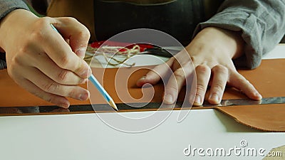 A shoemaker draws a line with a pencil on a large piece of genuine leather to cut it off. The process of creating Stock Photo