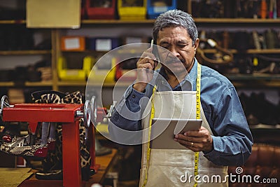 Shoemaker using digital tablet while talking on mobile phone Stock Photo